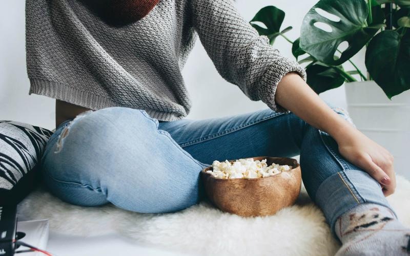 woman sits on a rug with a bowl of popcorn