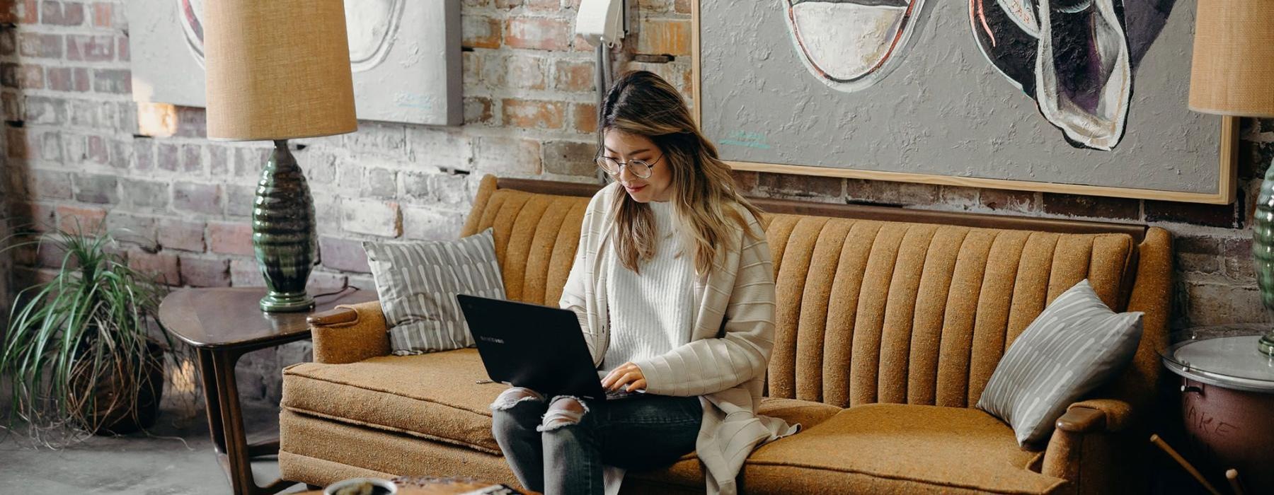 a woman sitting on a couch working on a laptop